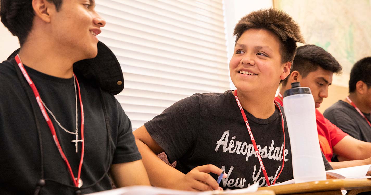 Academy student smiles while sitting in a classroom at a table