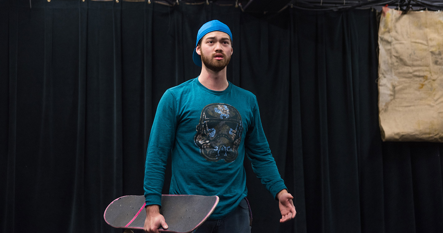 Student holding skateboard performs a monologue