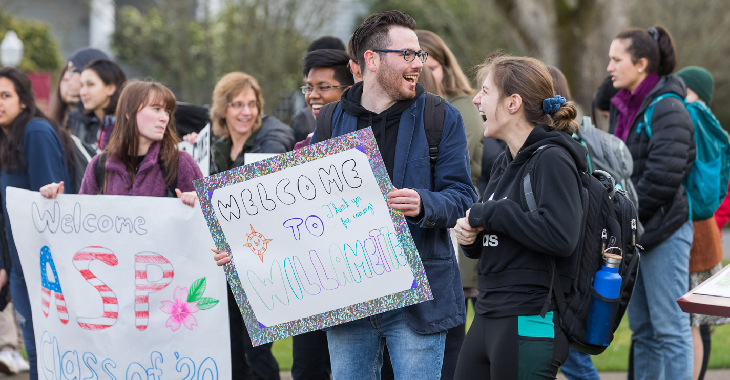 Students edge the sidewalk by Sparks parking lot smiling and holding welcome signs