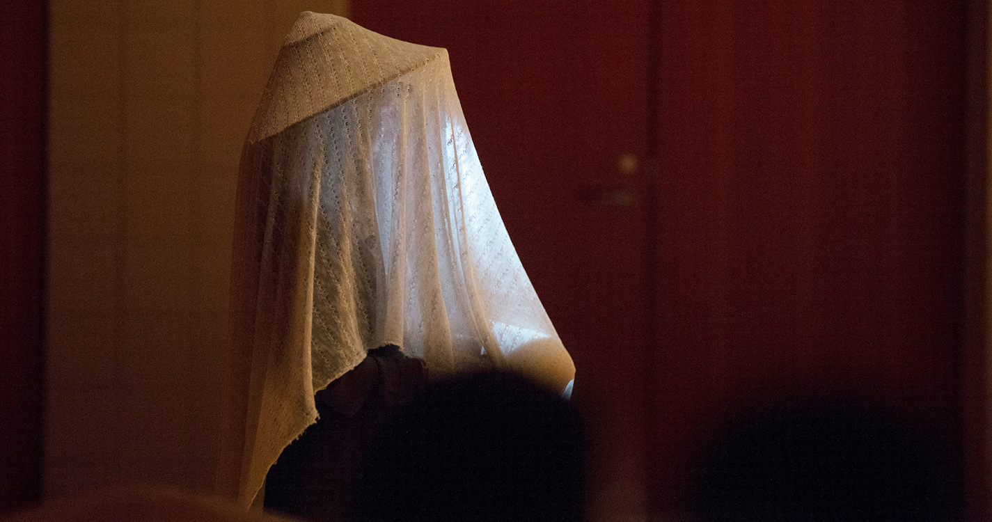 A performer with a lacy white blanket draped over their head and body