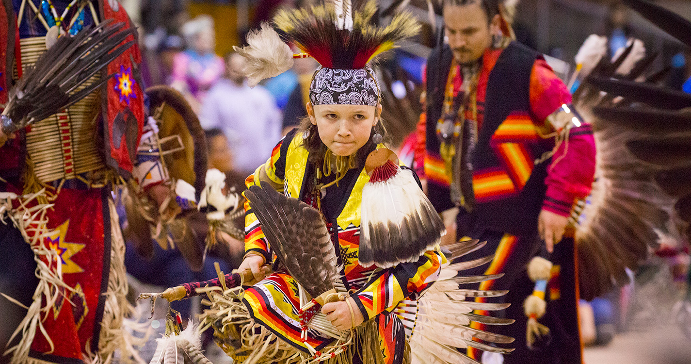 A child wearing bright multi-colored regalia dances at the annual Social Pow wow.