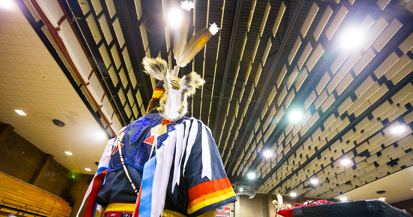 In the foreground of the gymnasium’s rafters, a man dressed in traditional regalia dances in the annual Social Pow wow.