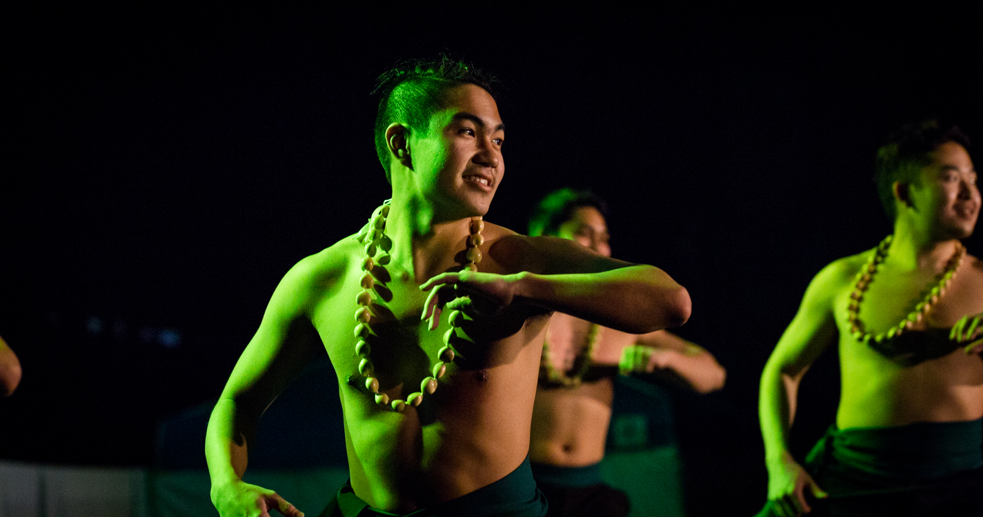 men wearing beaded necklaces dance in green light