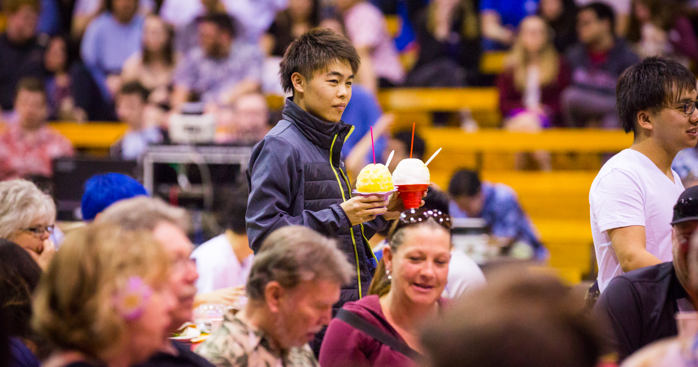 a student holds Hawaiian shaved ice in the midst of a crowded gymnasium
