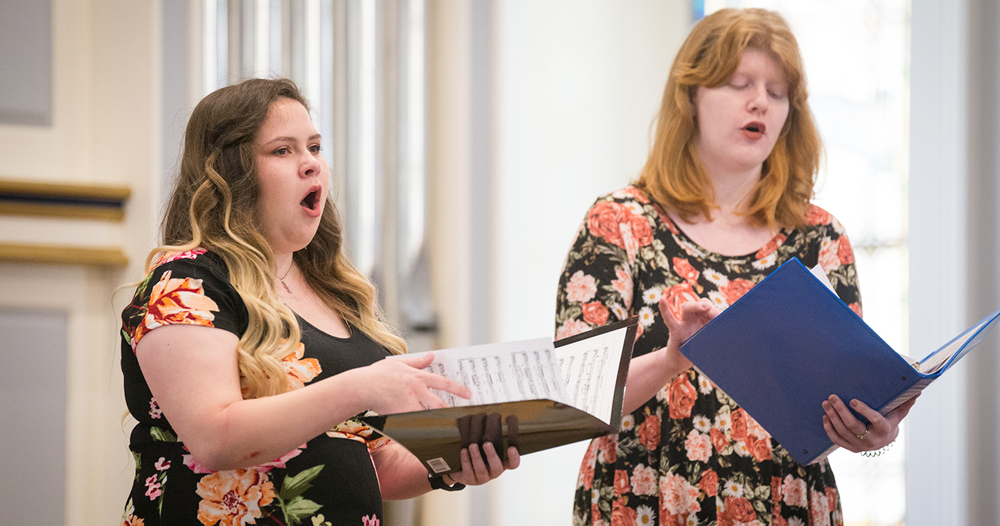 Two students hold music and sing at Student Scholarship Recognition Day. 
