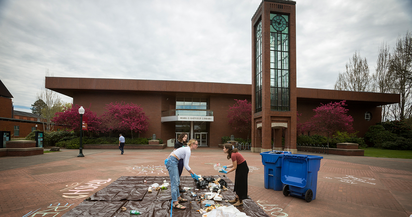 Students wearing rubber gloves sort trash from recycling on a tarp in Jackson Plaza.