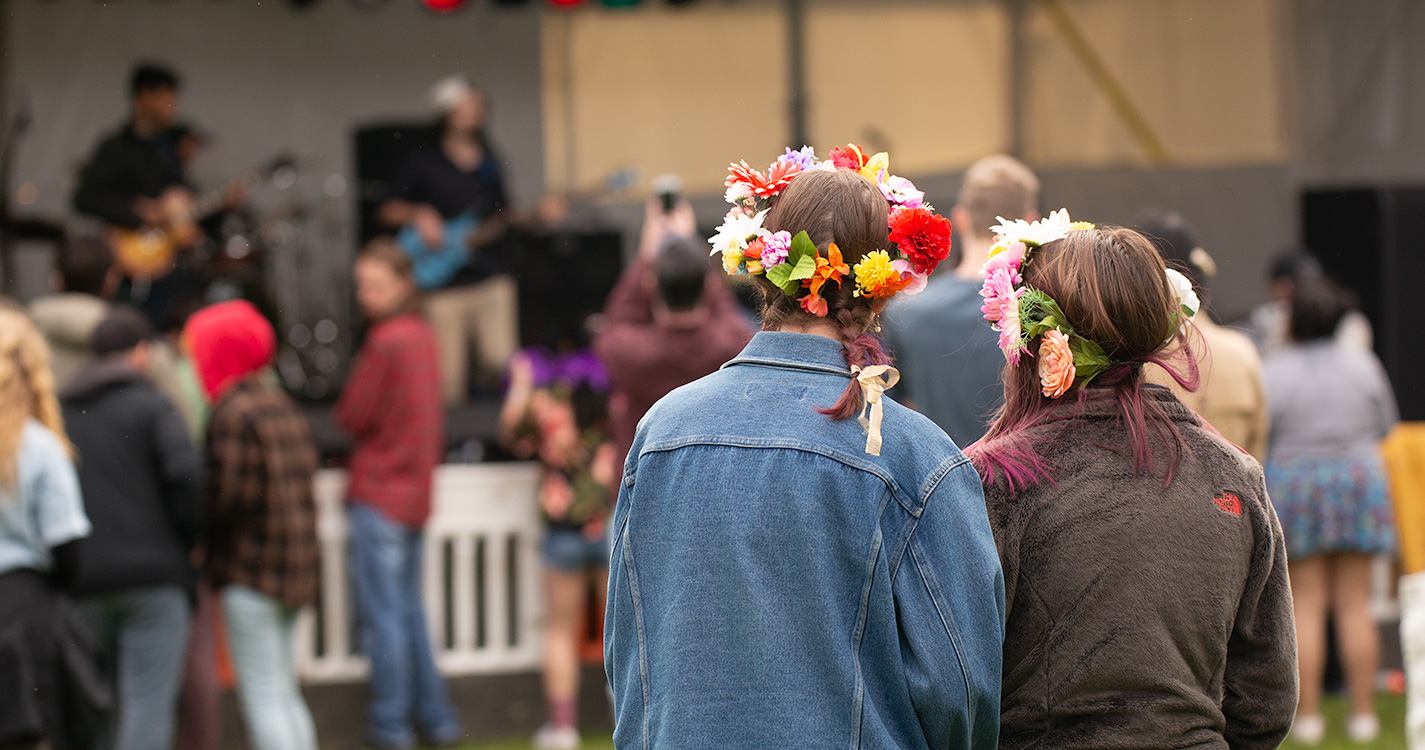 Two students with flowers in their hair look toward the Wulapalooza stage.