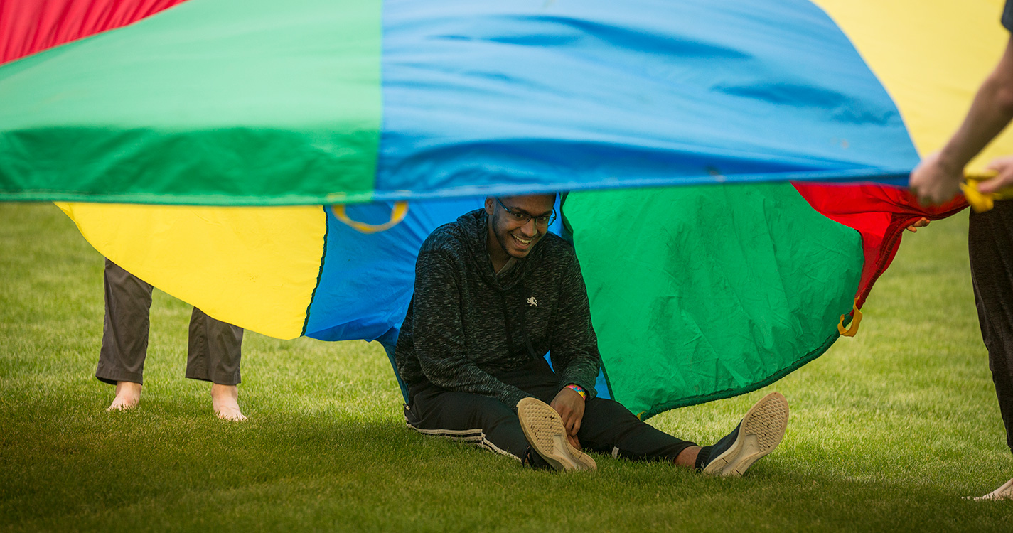 A student sits in the grass under a brightly colored parachute