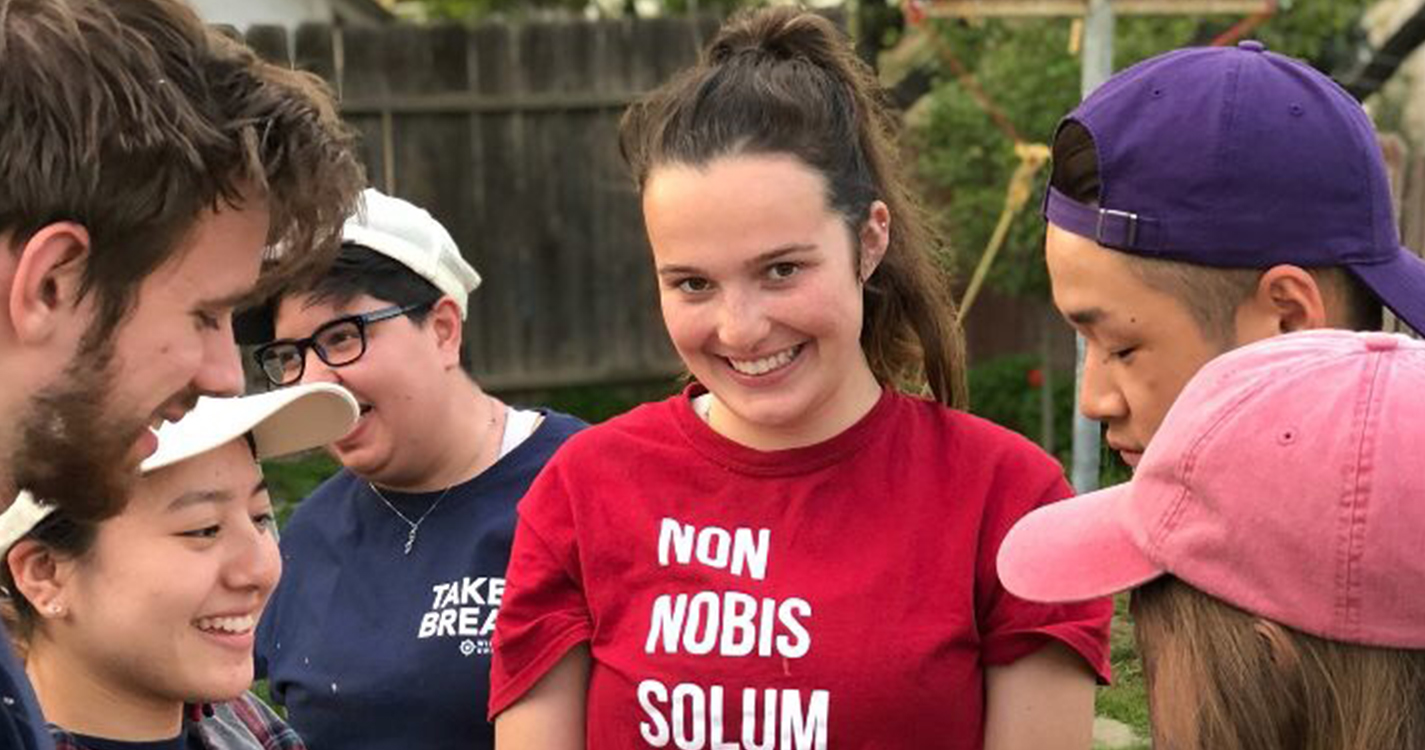 A student smiles wearing a shirt with the words "Non Nobis Solum" on it.