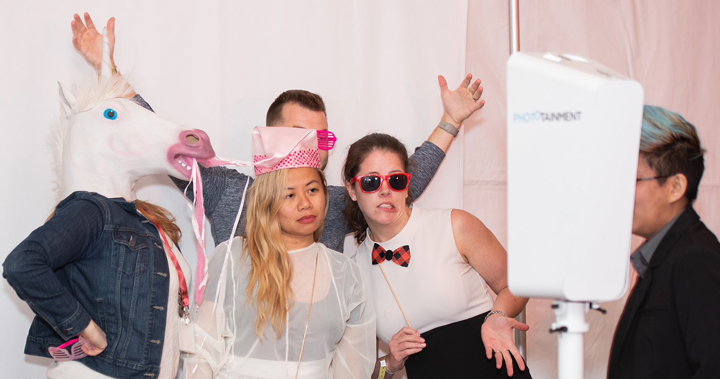 four alumni do a goofy pose in a photo booth, one wears a white horse head