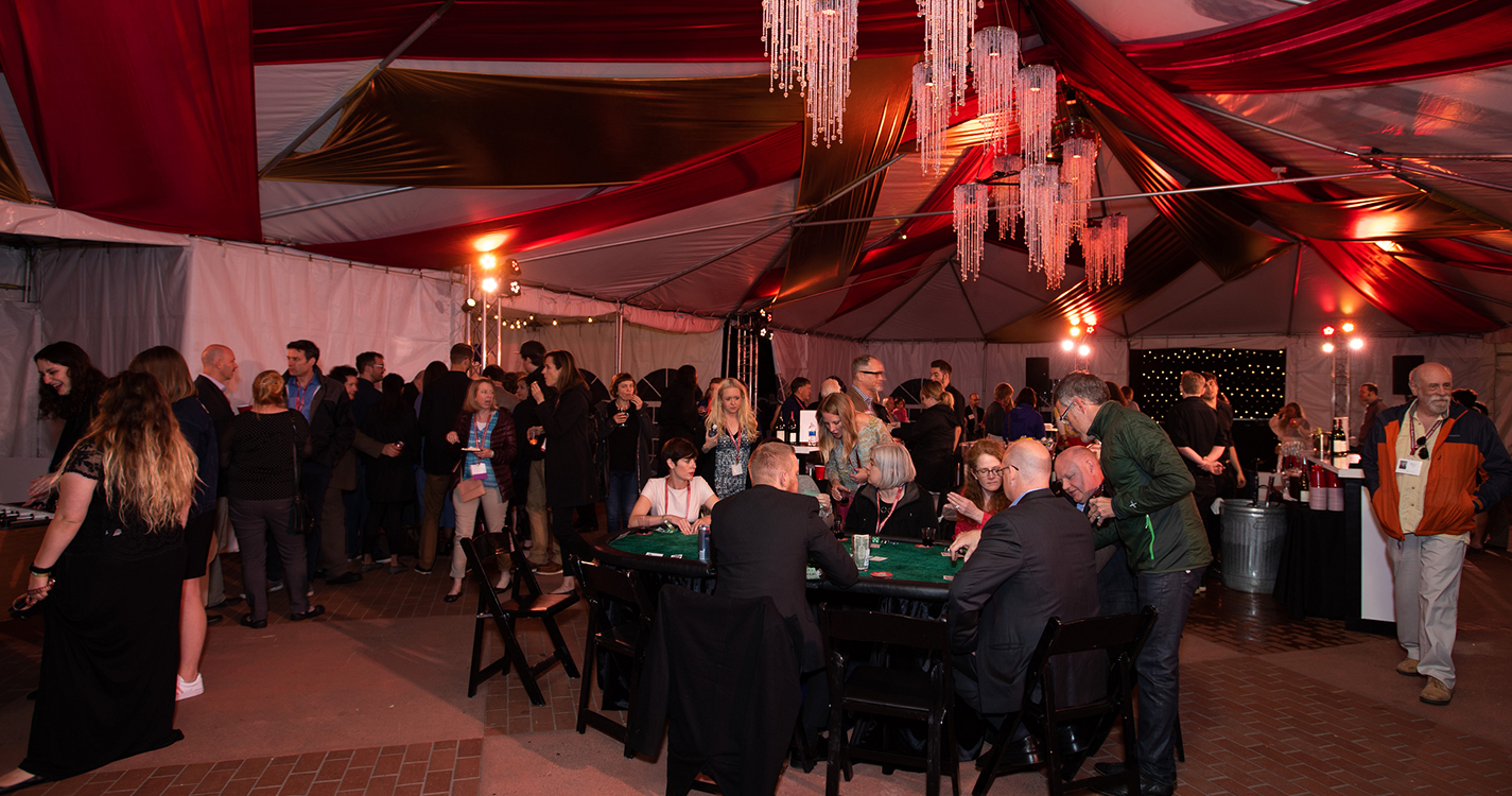 chandeliers light a tent over tables of alumni eating a meal