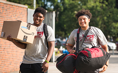 Two football players carry bags during move-in of Opening Days