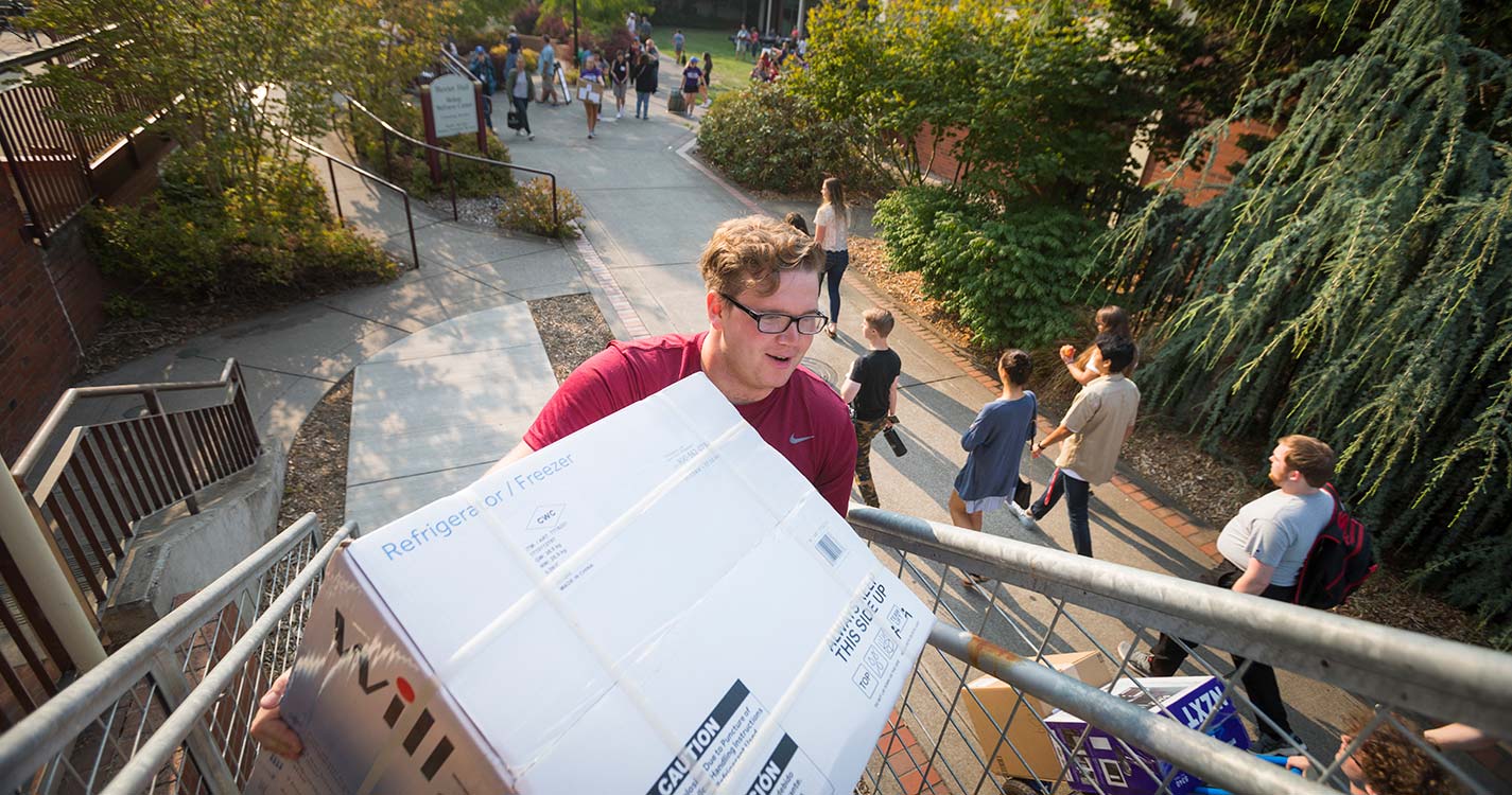Student carries a large box up stairs during Opening Days move-in.