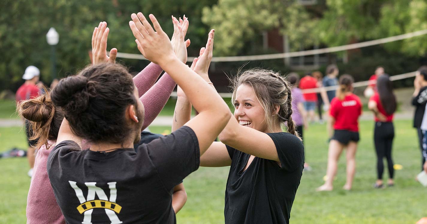 Three students high-five one another on a volleyball court on the Quad.