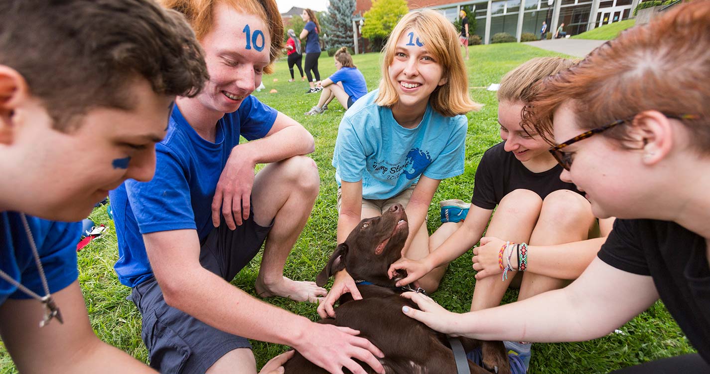 five students pet a chocolate lab on the Quad