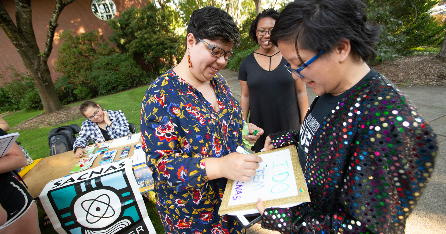 Assistant Professor Rosa Leon Zayas signs a white board a student is holding at the SACNAS table