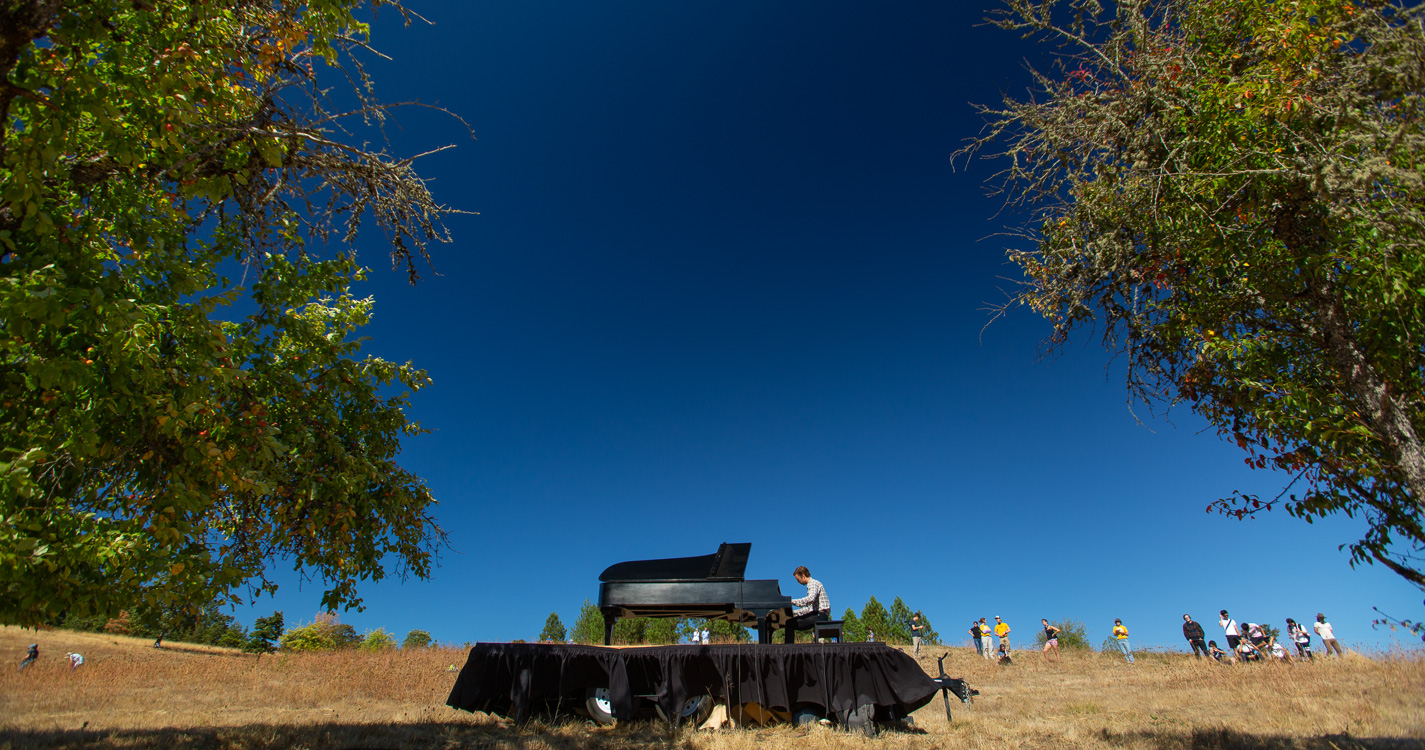 Hunter Noack plays a grand piano in the middle of a field at Willamette's Zena campus