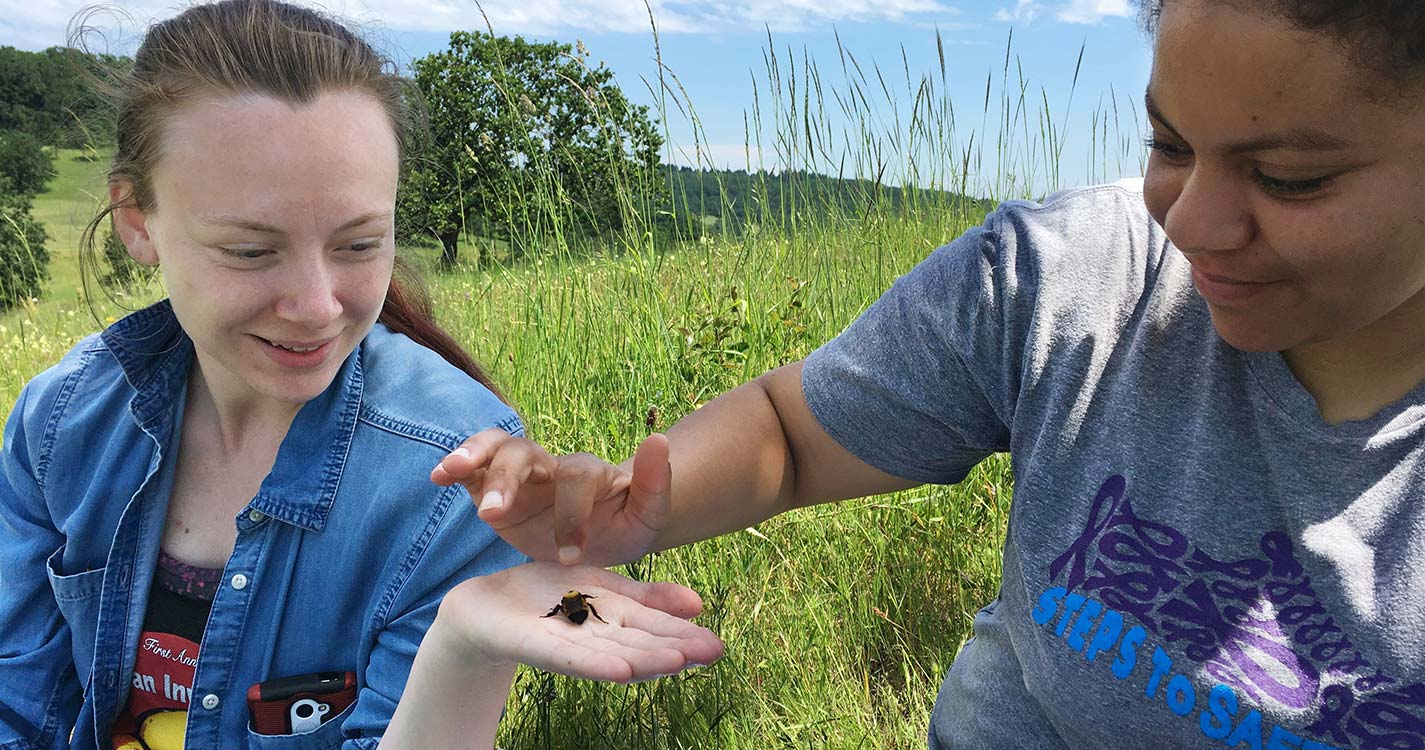 One student holds a bee in her palm, while another student gently touches the bee