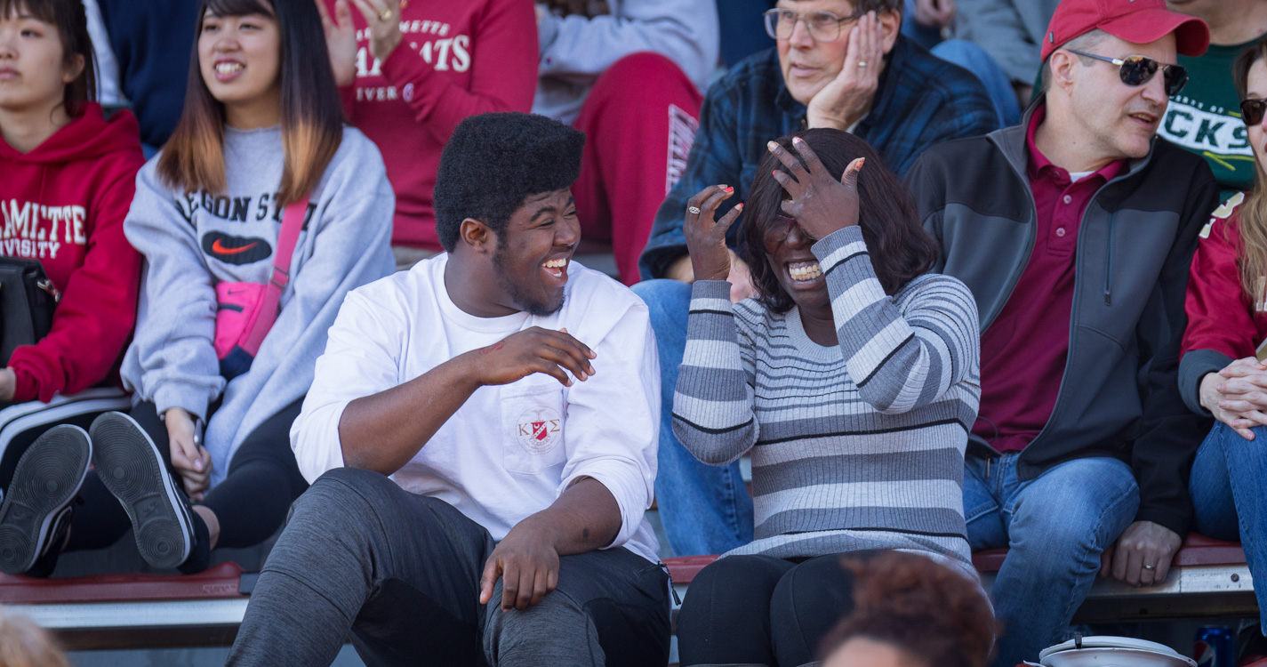 Two people smile and laugh amid the Bearcat fans at a football game