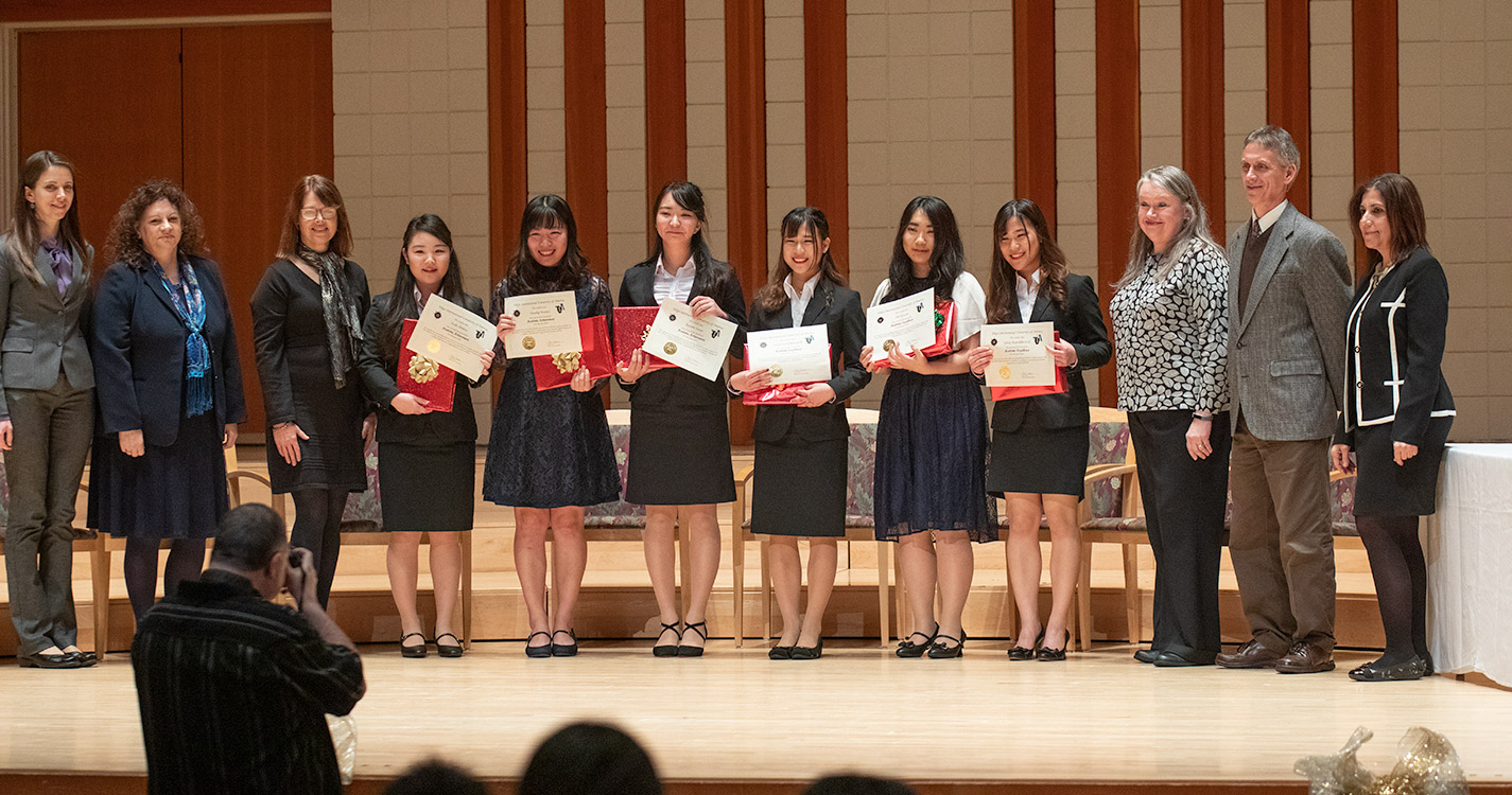 Students stand in a line on stage holding up their award certificates