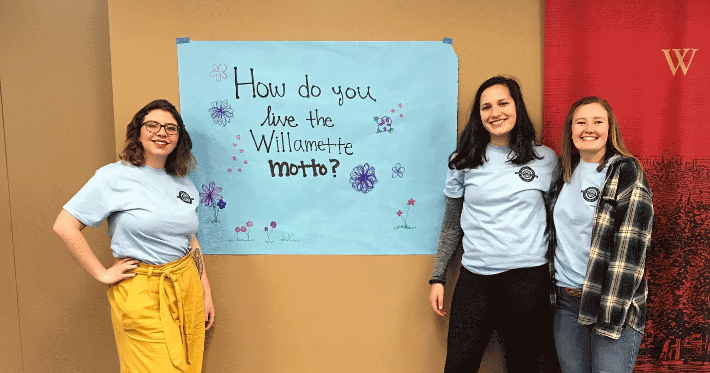 Students stand in front of sign reading “How do you live the Willamette Motto?”