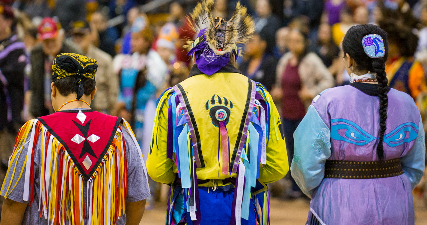 view from behind of three people wearing colorful garments with diamond shapes on one, bear claw and eyes on the others