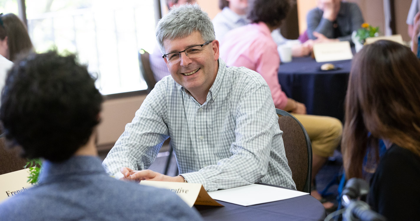 professor smiles while seated at a table