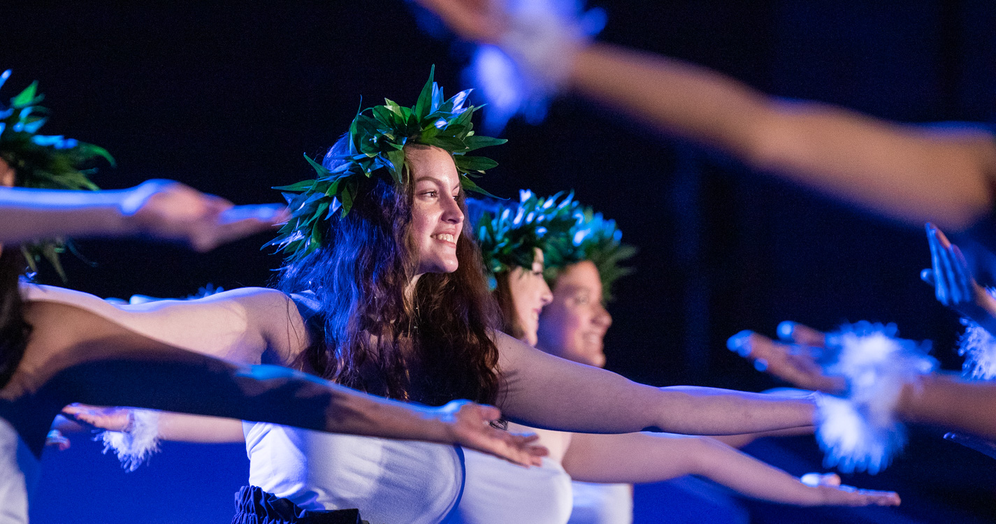 Student with a crown of leaves and white shirt dances with arms outstretched