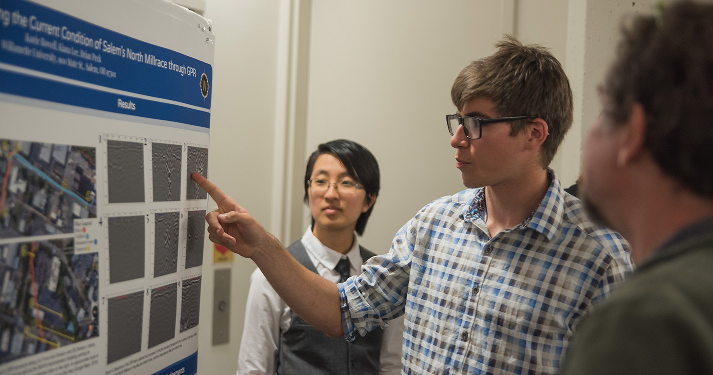 Student points at a photo of research on a poster while two other listen
