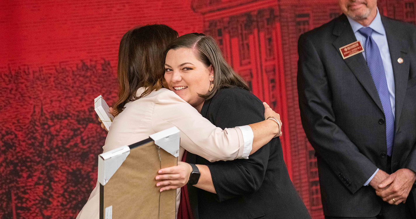 Student receives hug from staff member when receiving award
