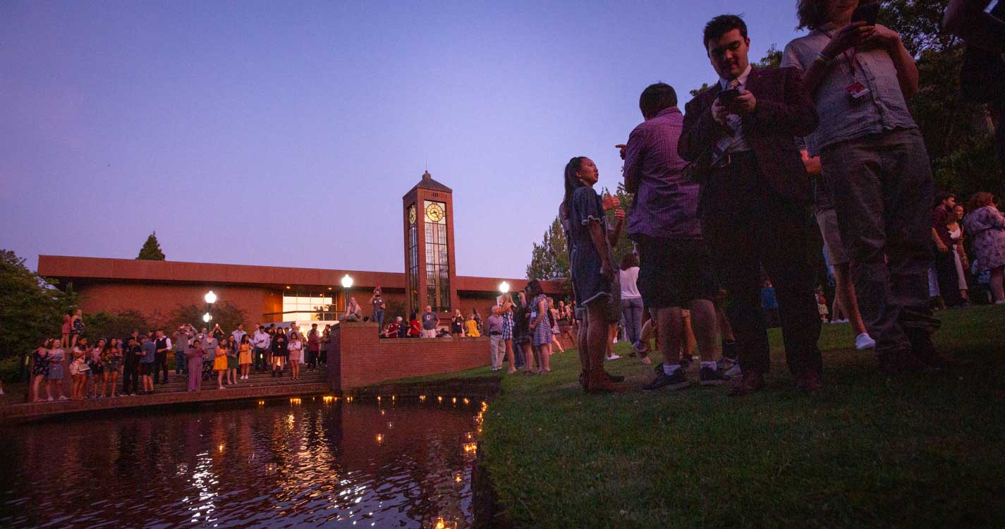 Students line the Mill Stream at dusk as candles float on the surface