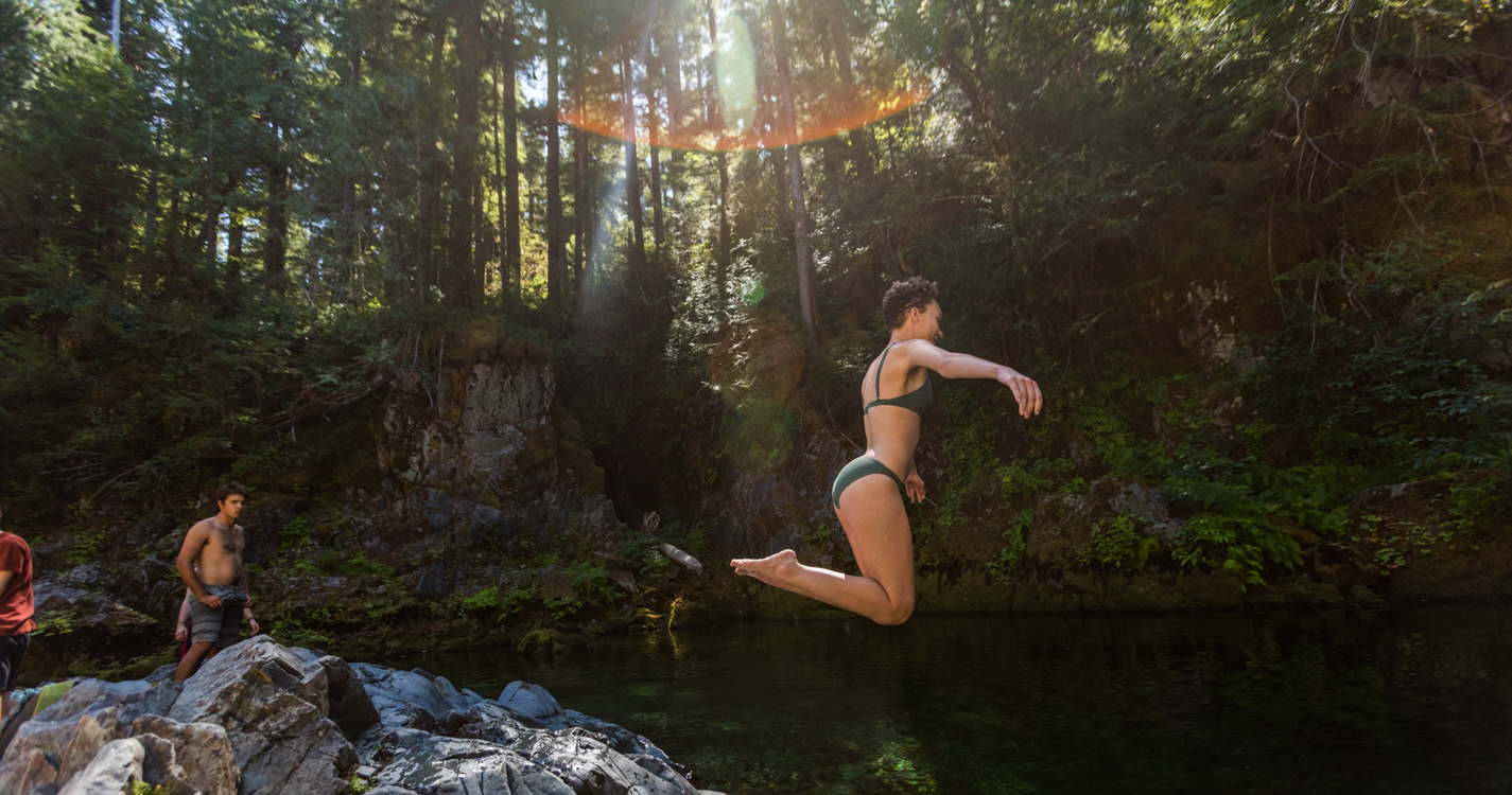 A student leaps from a cliff into Opal Creek as others watch