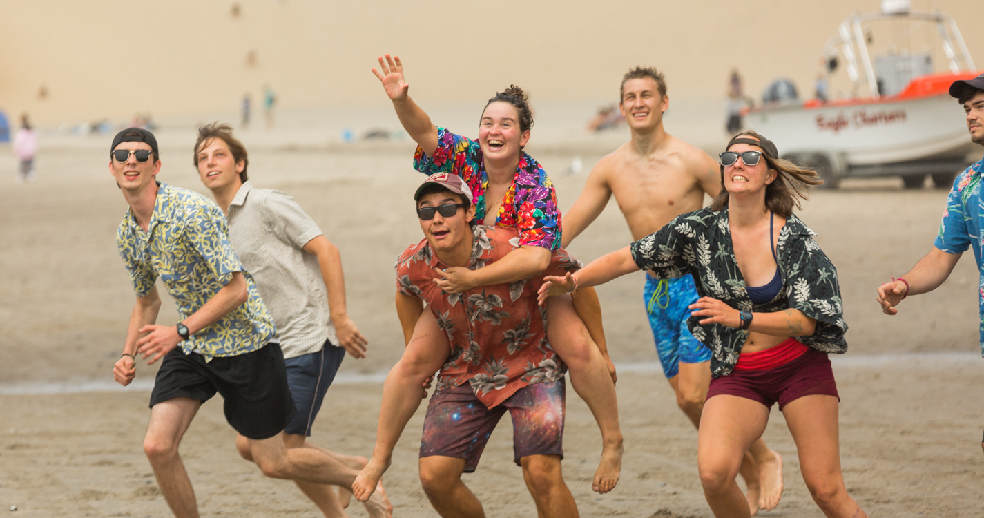 On the beach, students reach and leap for an incoming Frisbee