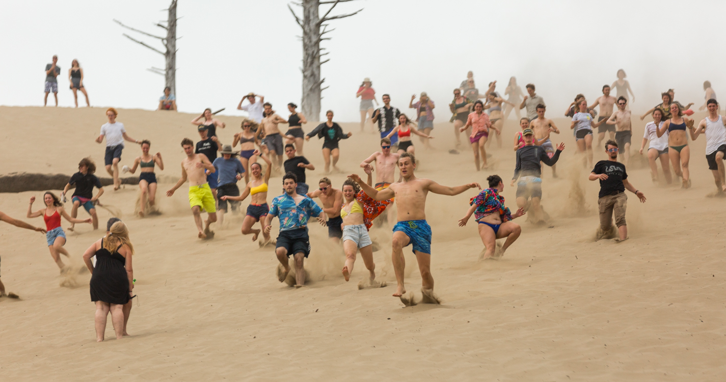 A group of more than 30 students run down a large sand dune in Pacific City