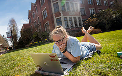 Student sitting on lawn working on laptop