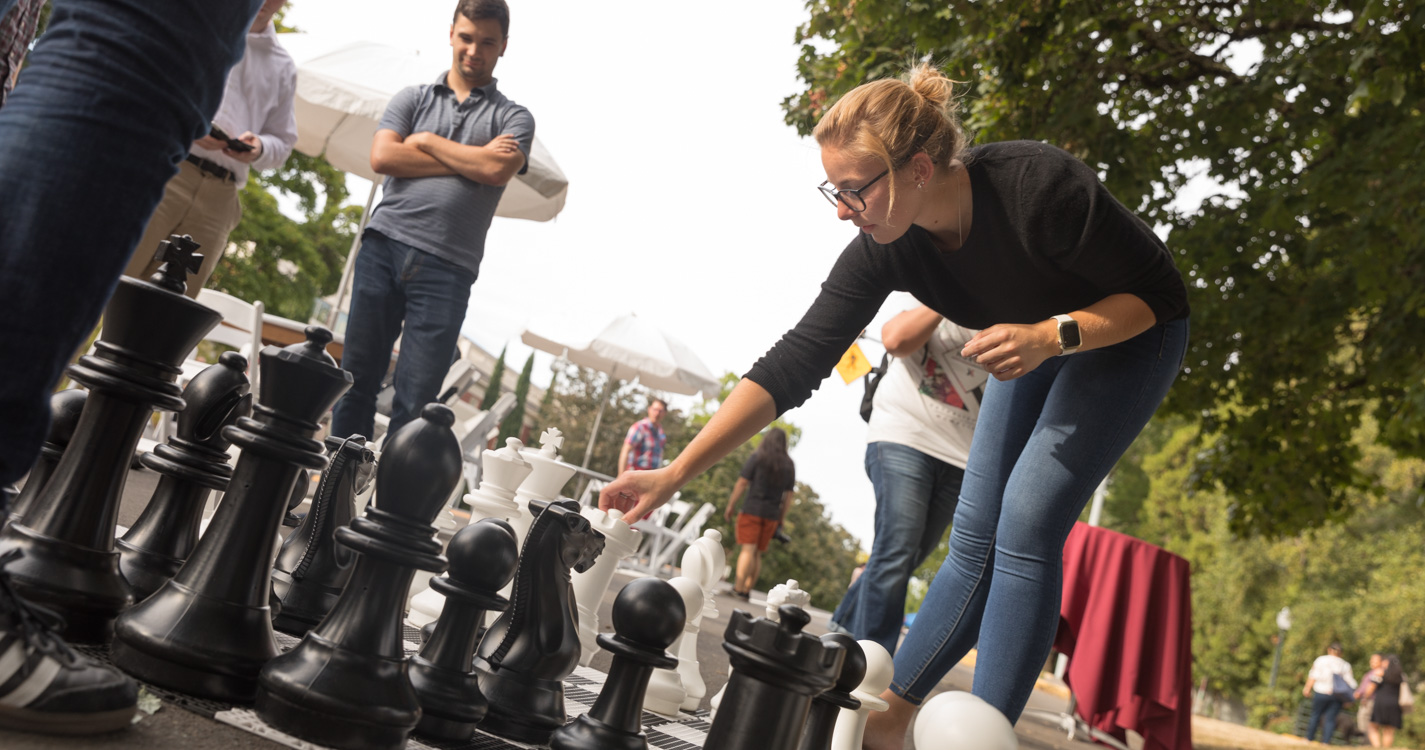 A student reaches down to move a chess piece on a board with knee-high pieces
