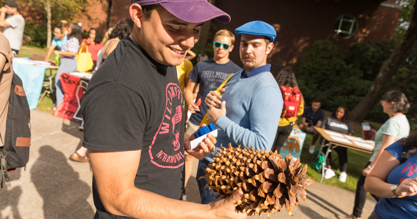 A student holds a pine cone that is slightly larger than a football