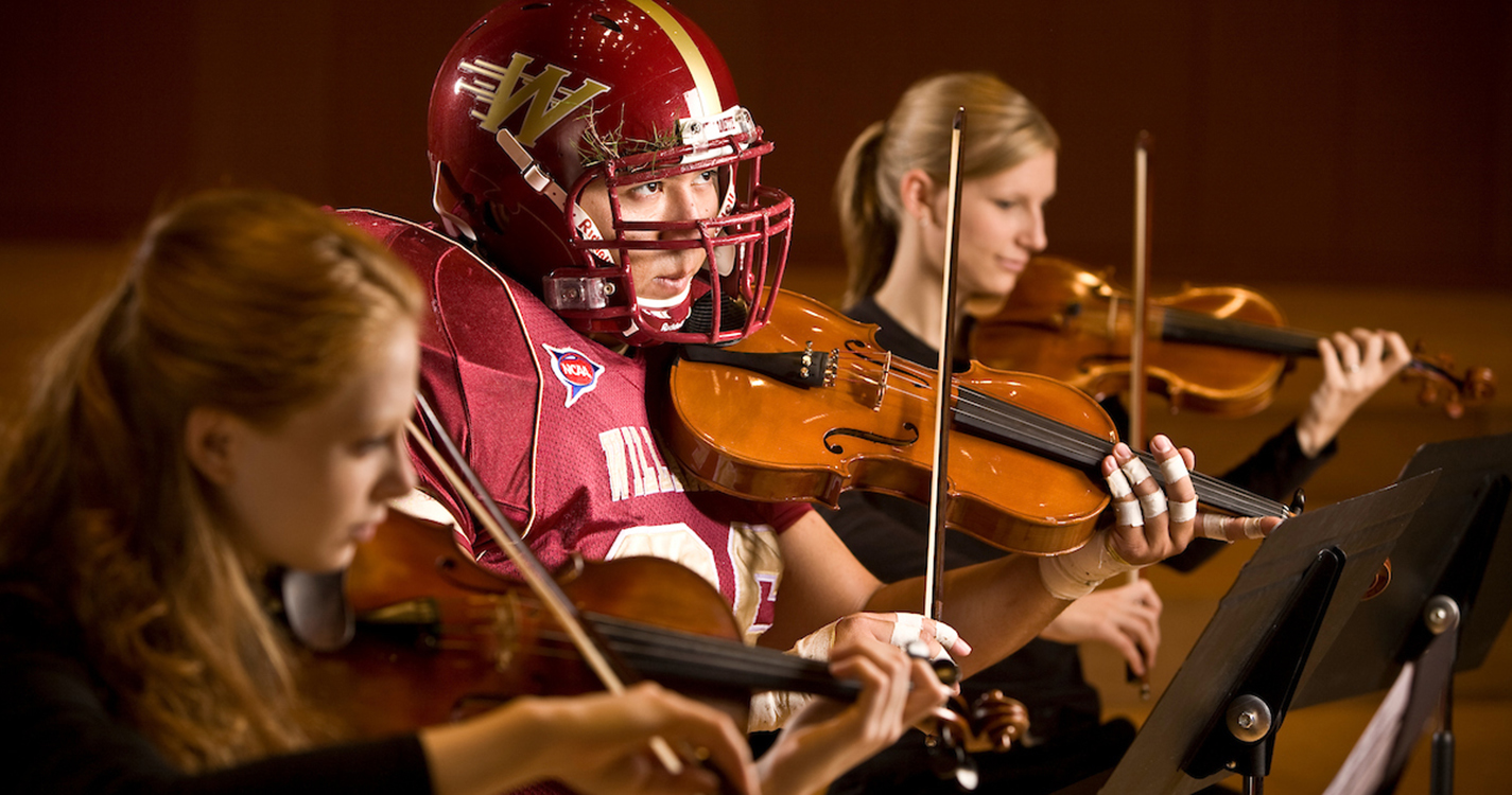 Student wearing a football costume plays a violin