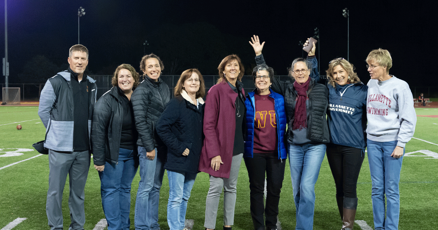 A group of hall of fame awardees pose together on the football field at half time
