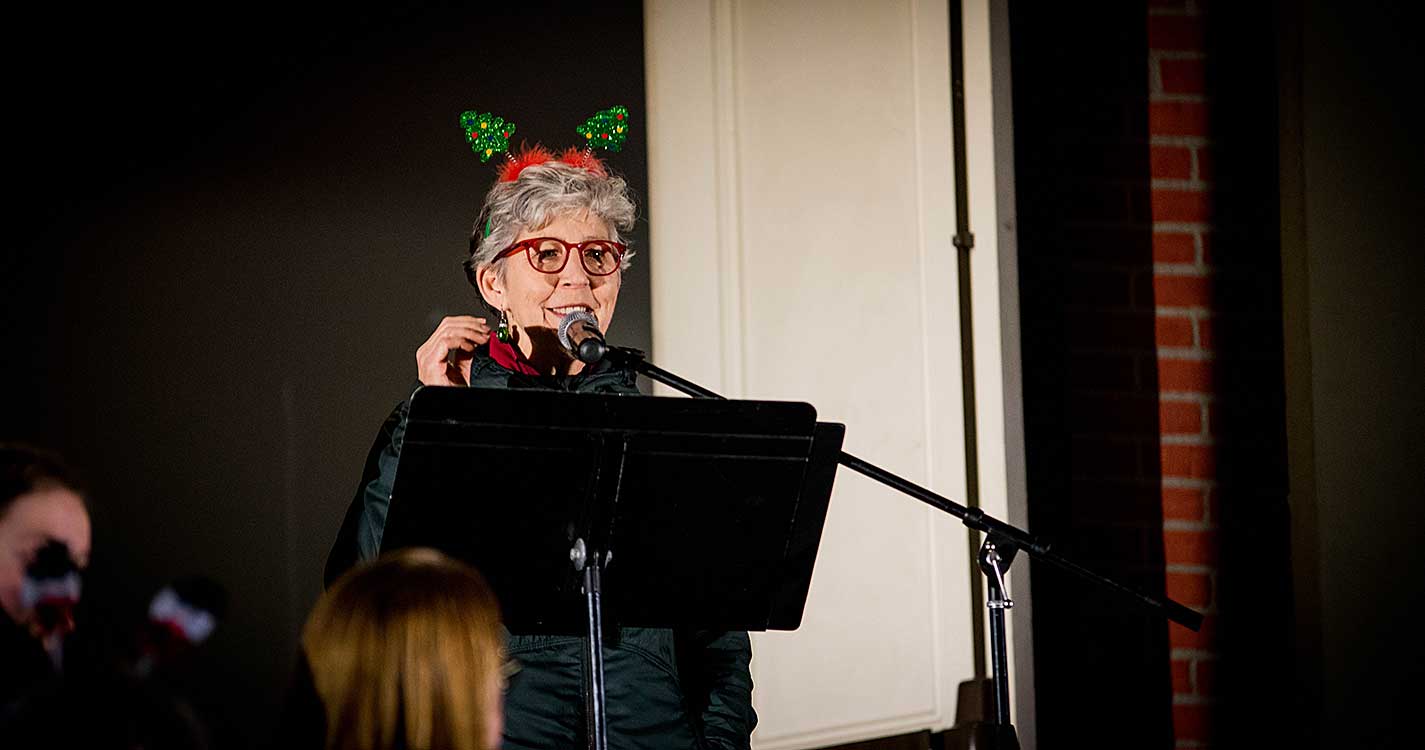 Chaplain Karen Wood adorned with two small Christmas trees like antlers welcomes the crowd gathered before Waller Hall