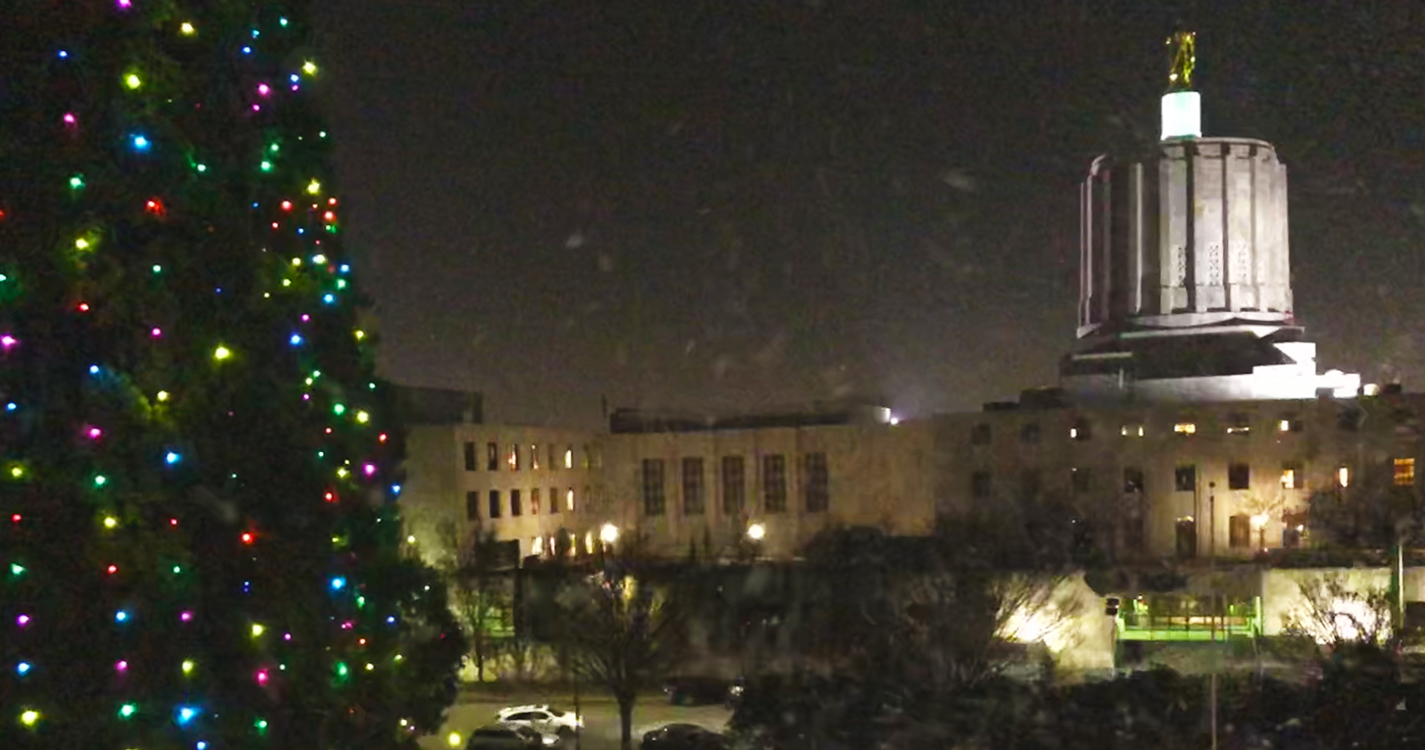 Star trees illuminated by colorful holiday lights with the Oregon State Capitol at night with fake snow falling
