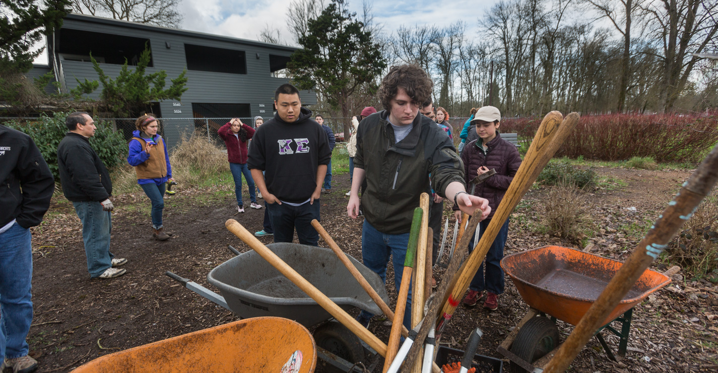 Students pull shovels and tools from a wheelbarrow at a community garden