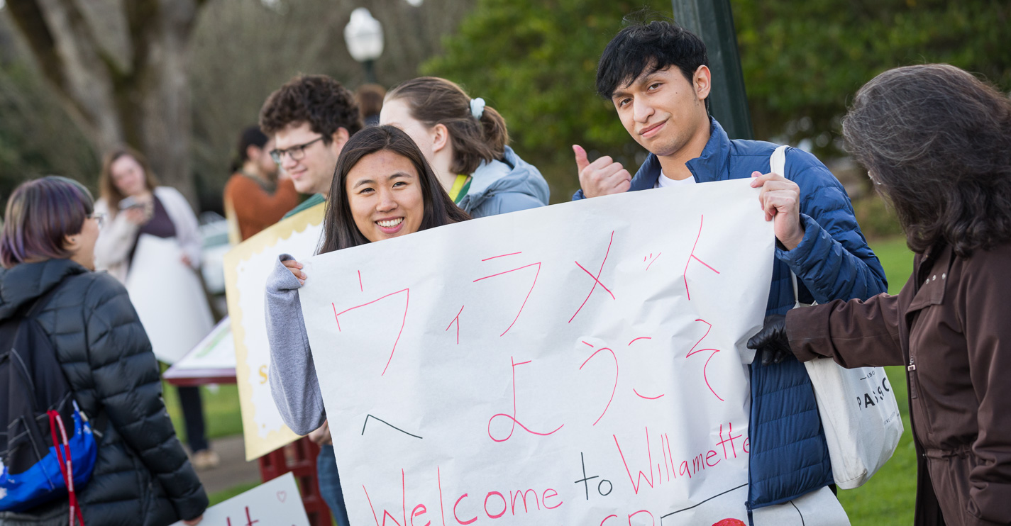Two students hold a sign saying "Welcome to Willamette" in both English and Japanese