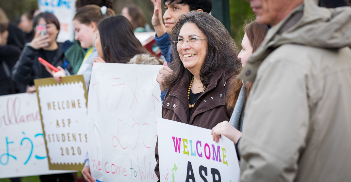 Joyful students and employees line the sidewalk by Sparks parking lot smiling and holding welcome signs