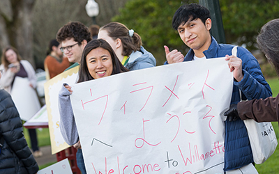 Two students hold a sign saying "Welcome to Willamette" in both English and Japanese
