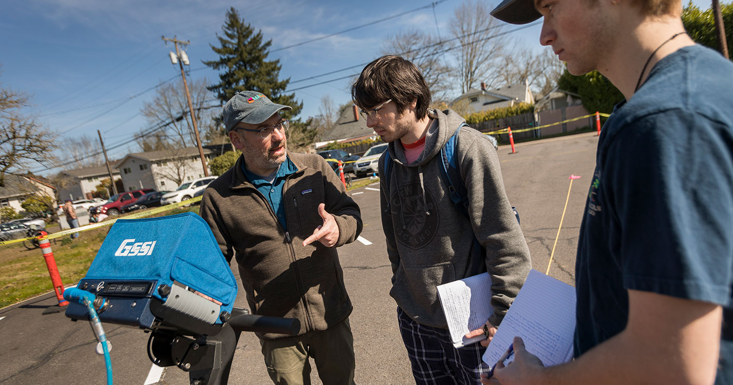 Scott Pike, professor of environmental science and archaeology, speaks to two students. 