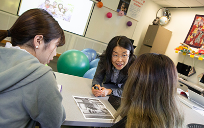 A professor leans into a table in the World Languages Studio to provide instruction to two students