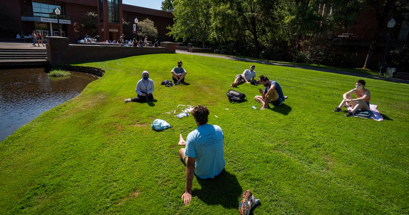 Students practicing social distancing on lawn in front of the Mill Stream