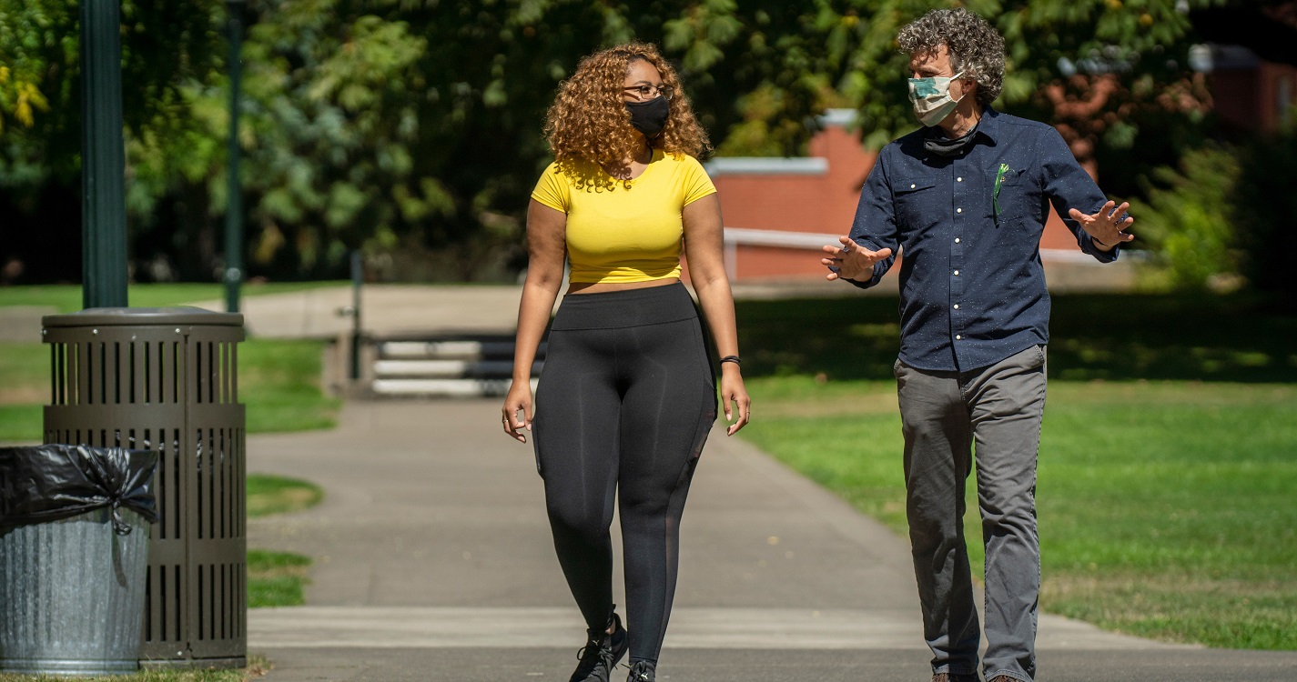 Professor David Craig and a student talking on sidewalk with masks on
