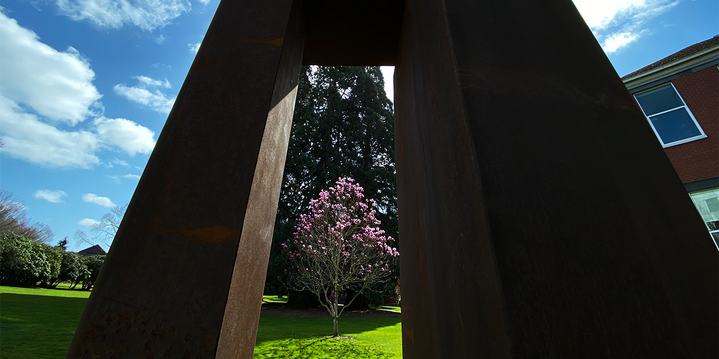 View of pink flowering tree through the columns of the 15-foot tall sculpture